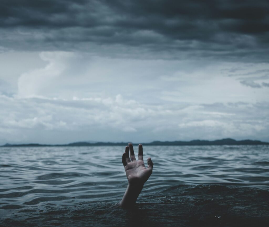 main sortant de l'eau sous un ciel orageux, symbolisant la détresse et la lutte contre le burn-out